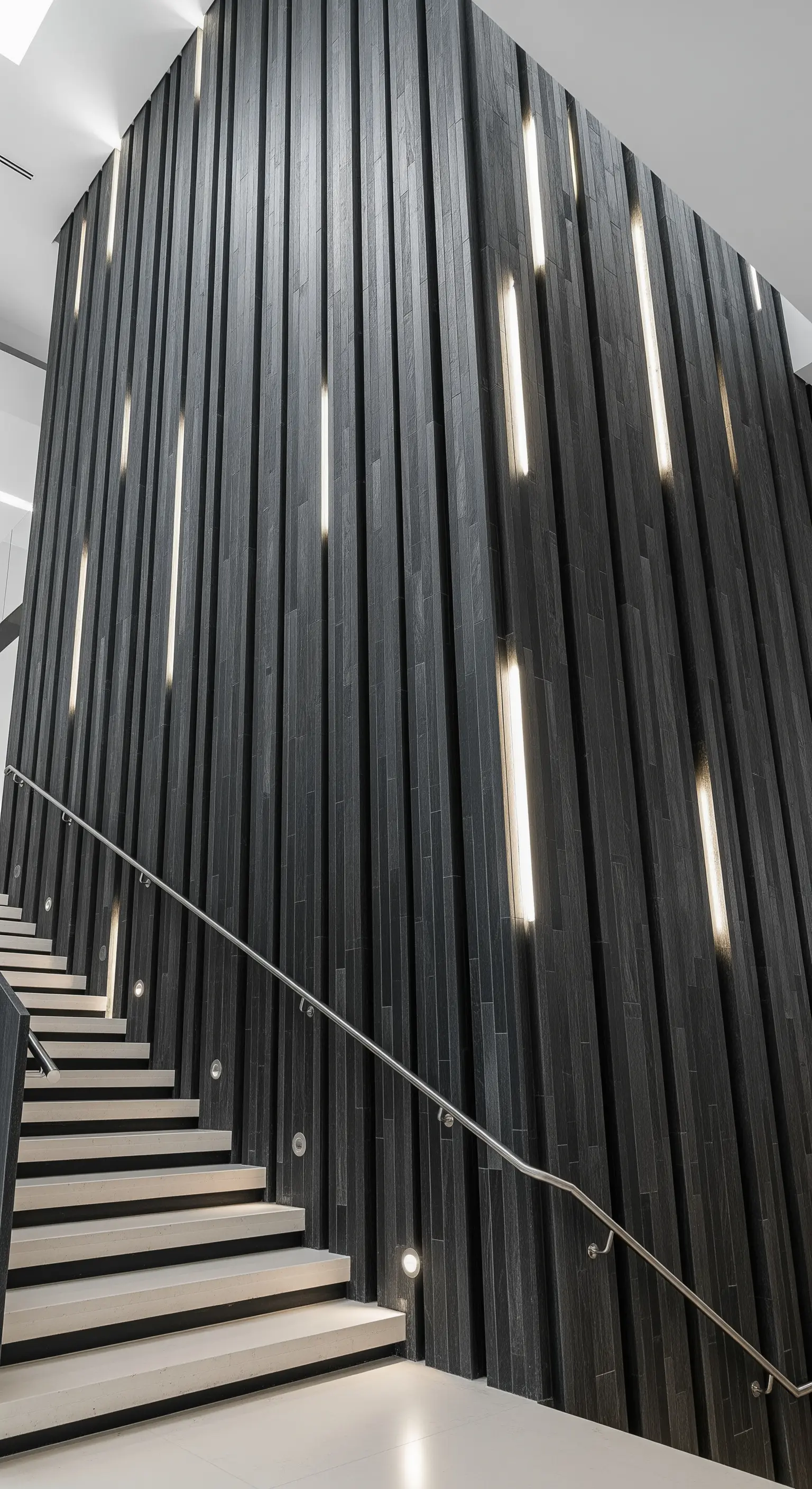 Modernes Treppenhaus mit hoher Wand aus dunklen, vertikalen Paneelen und integrierten Leuchten.