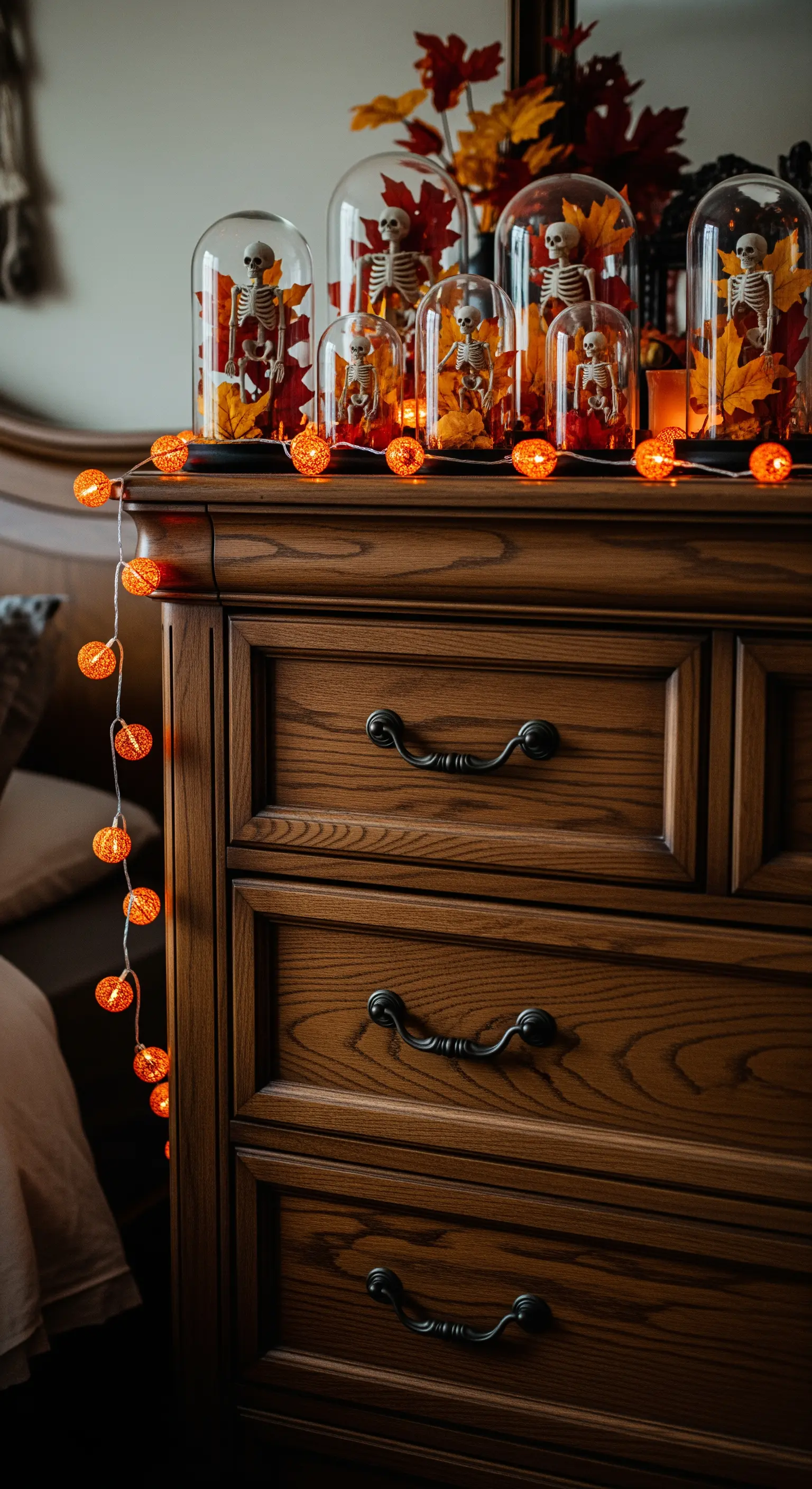 Holzkommode mit Glasglocken, Mini-Skeletten, Herbstblättern und oranger Lichterkette