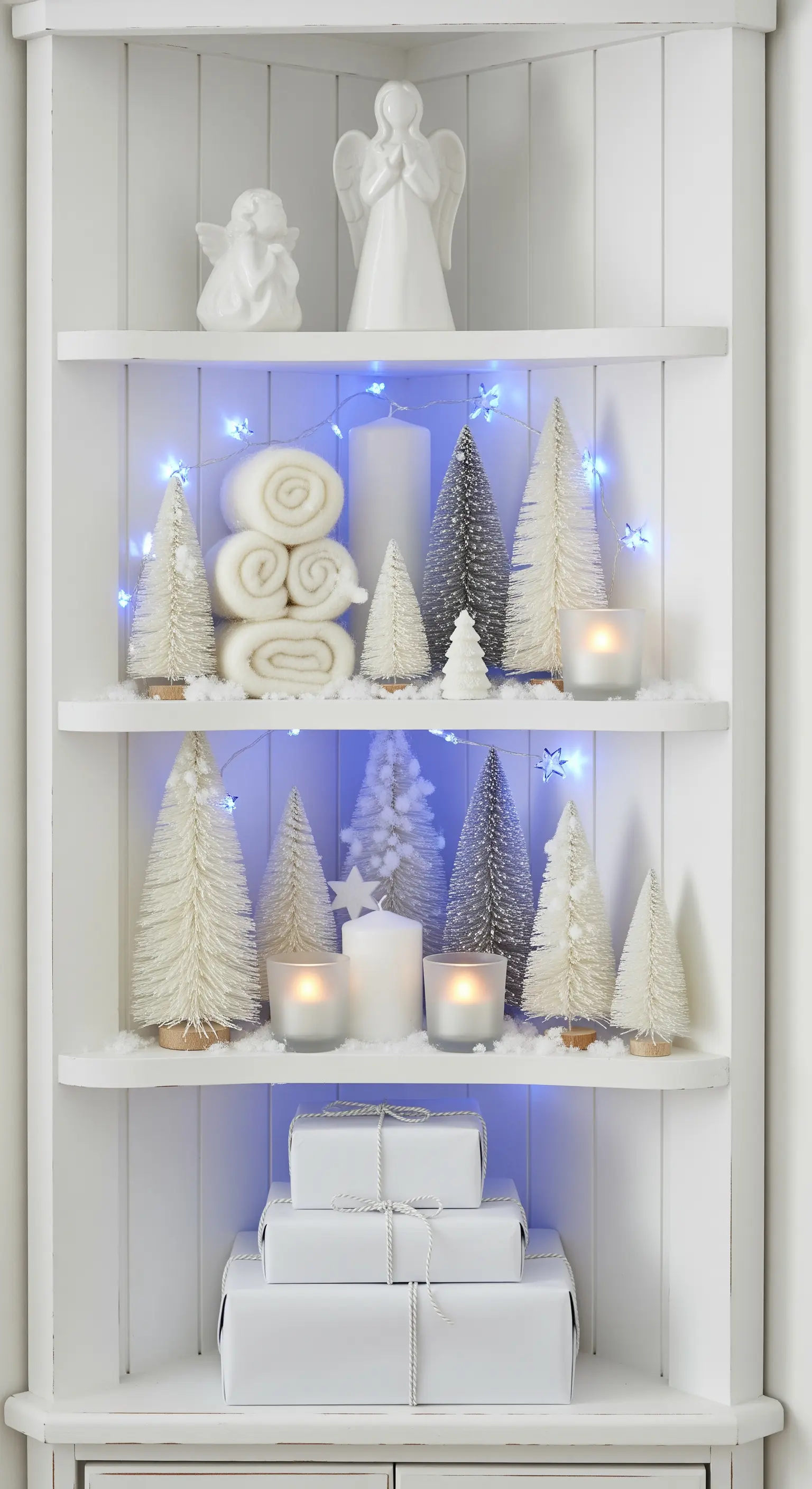 Weißes Eckregal mit weißen Deko-Bäumen, Kunstschnee und blauer Lichterkette