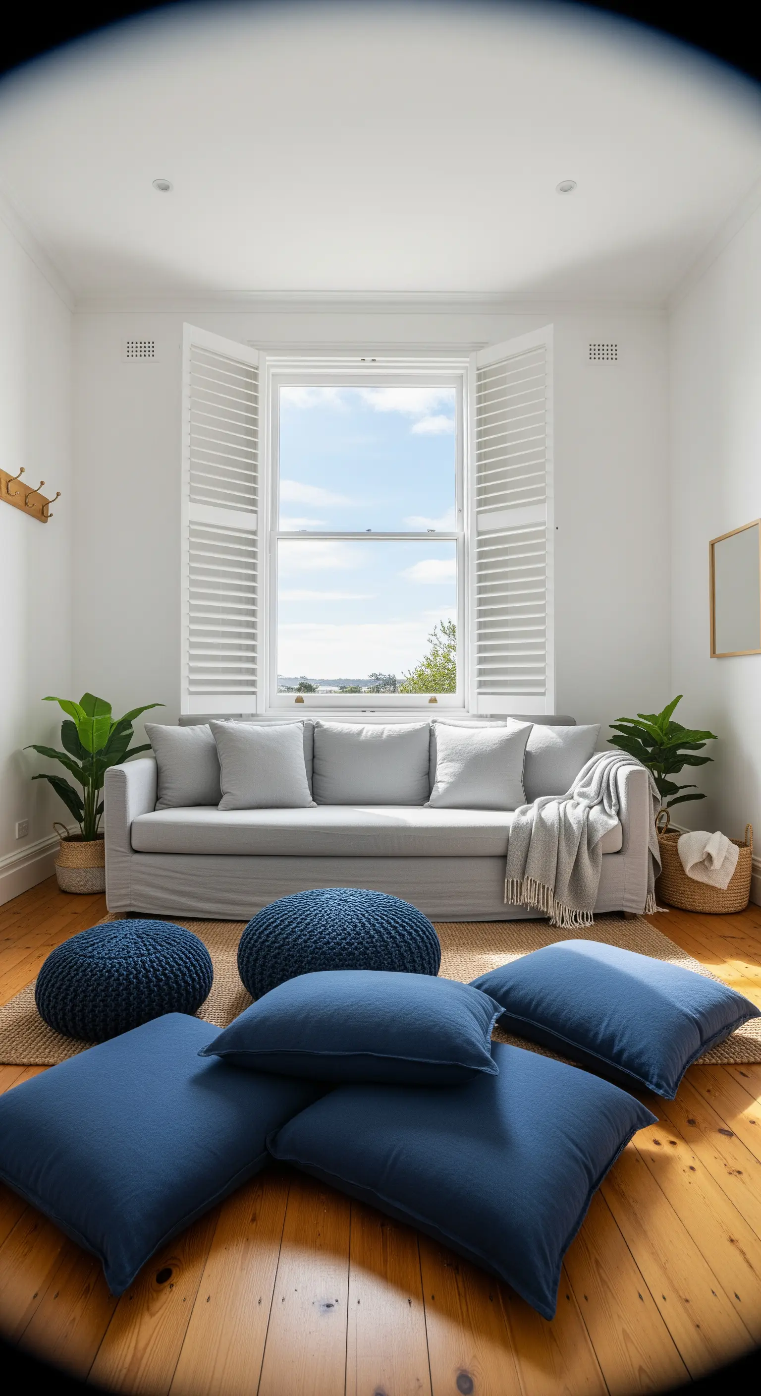 Wohnzimmer mit hellgrauem Sofa, blauen Bodenkissen, Juteteppich und Grünpflanzen.