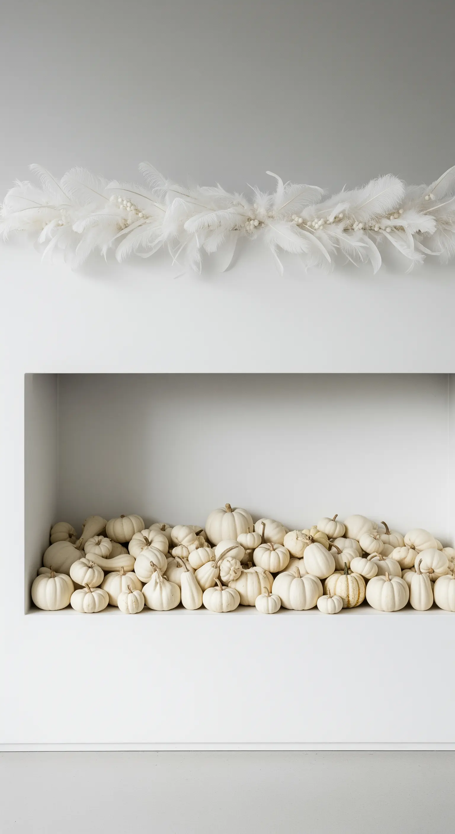 Weiße Nische gefüllt mit zahlreichen kleinen weißen Kürbissen und Federgirlande