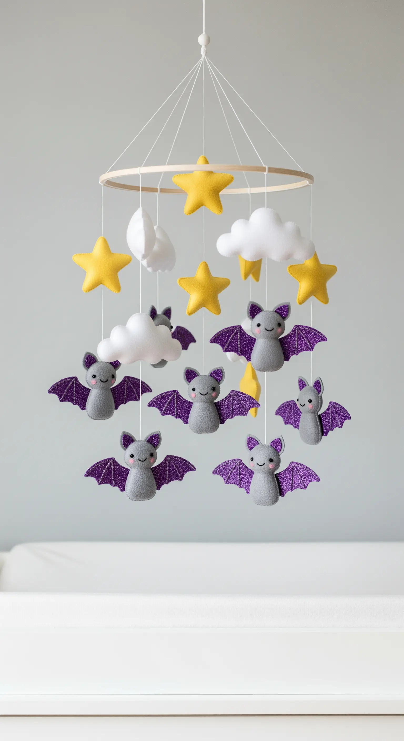 Ein handgemachtes Mobile mit niedlichen Fledermäusen, Sternen und Wolken aus Filz über einem Babybett.